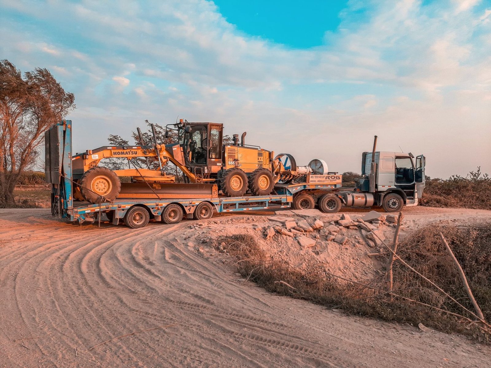 Heavy machinery loaded on flatbed trailers at a dusty site