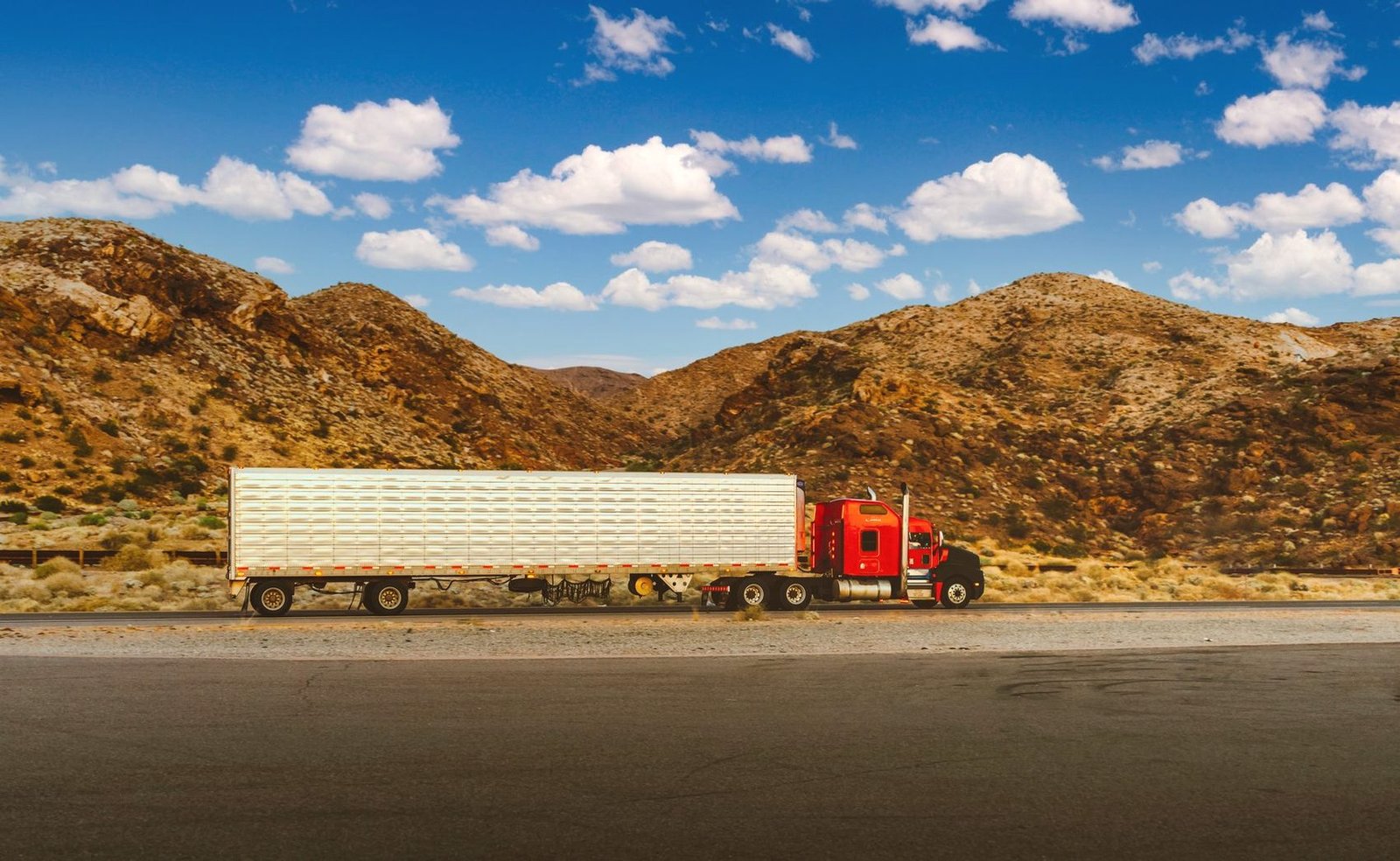 Refrigerated trailer rig on a desert highway below dry hills
